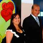 Nesta foto, da esquerda para a direita, veem-se uma mulher de vestido preto, um homem de terno escuro e uma mulher de vestido vermelho. Todos sorriem para a câmera. Atrás da primeira mulher, nota-se um banner com o desenho de dois corações sorridentes dentro de uma camisinha.