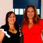 Nesta foto, veem-se duas mulheres posando para a câmera. Percebe-se que uma está de vestido preto e a outra de vermelho. Próximo à primeira mulher, nota-se um banner com o desenho de dois corações sorridentes dentro de uma camisinha.