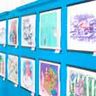 Esta foto em perspectiva revela exposição de cartuns afixados lado a lado em uma parede azul.