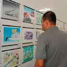 Um homem observa parede repleta de cartuns nesta foto em cores. Ele está de costas para a câmera e a imagem está em perspectiva.