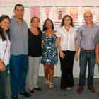 Nesta foto em cores, um grupo de pessoas posicionadas lado a lado posa para a câmera. Nota-se que estão em uma sala fechada, na frente de uma parede repleta de cartuns. Algumas pessoas sorriem, mas a maioria tem feição fechada.