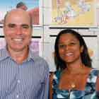 Em close, homem e mulher posam para a câmera estampando largo sorriso. Nota-se que a parede branca ao fundo foi preenchida com cartuns coloridos.