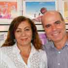 Em close, mulher e homem posam para a câmera e sorriem. Nota-se que a parede branca ao fundo foi preenchida com cartuns coloridos.