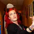 Nesta foto em ângulo fechado, observa-se um homem à extrema esquerda, de casaco azul. Ele olha para o cartum afixado em frente a ele, numa parede amarela. Logo à frente e abaixo da obra, encontra-se uma mulher de cabelos vermelhos olhando para o homem enquanto gesticula com as duas mãos. Ao longo do corredor, compondo o fundo da imagem, notam-se outras pessoas em pé, também apreciando os cartuns.