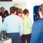 Esta foto revela pessoas visitando exposição de cartuns. Nota-se que as obras foram afixadas em estruturas verticais brancas. 