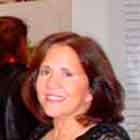 Nesta foto, percebe-se o interior de um local fechado e espaçoso. Em destaque, ao centro da imagem, há três mulheres em pé, lado a lado, e apenas a da direita olha para a câmera e sorri. Ao fundo, nota-se um painel imenso e colorido, que toma toda a extensão da parede. Logo abaixo, há estruturas brancas onde foram afixados cartuns coloridos, além de um grande texto.