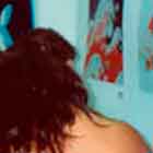 Nesta foto, percebem-se algumas pessoas observando de perto cartuns coloridos afixados numa estrutura vertical branca.