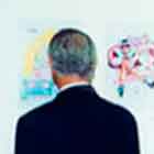 Esta foto revela dois homens de costas para a câmera. Percebe-se que eles observam cartuns coloridos afixados em painéis brancos.