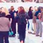 Esta foto revela pessoas visitando exposição de cartuns. Nota-se que as obras foram afixadas em estruturas verticais brancas e que a parede ao fundo é, na verdade, uma tela gigantesca.