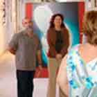 Nesta foto há algumas pessoas olhando em direção ao fundo da imagem. Neste sentido, encontra-se uma mulher que aparenta falar com essas pessoas. Atrás dela, notam-se algumas estruturas verticais vermelhas onde foram afixados cartuns coloridos. Observa-se ainda que a foto foi tirada em local amplo e fechado. 