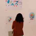 Esta foto em cores mostra pessoas à esquerda olhando cartuns afixados na parede.