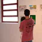 Nesta foto, percebe-se um jovem observando cartuns coloridos afixados na parede branca.