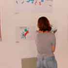 Nesta foto, percebe-se um grupo de quatro mulheres observando cartuns coloridos afixados na parede branca.