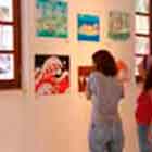 Nesta foto, percebe-se um grupo de quatro mulheres, à esquerda, observando cartuns coloridos afixados na parede branca.