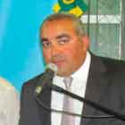 Nesta foto em cores, um homem está em pé, atrás de um púlpito, falando ao microfone. Ao fundo, notam-se duas pessoas e um grande banner atrás deles e a sigla “SEAP”. 