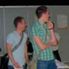 Nesta foto em cores, veem-se alguns rapazes passando em frente a exposição de cartuns. Percebe-se que um deles leva uma das mãos ao queixo enquanto observa uma das obras.