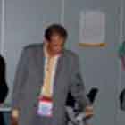 A foto em cores revela algumas pessoas observando painéis que abrigam cartuns. Nota-se que outras pessoas param em frente a mesas que contêm materiais impressos.