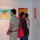 Esta foto mostra visitantes da mostra observando painéis preenchidos com alguns cartuns coloridos. 