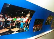 A foto mostra corredor decorado com fotografias impressas em fundo azul, ocupando parte da parede à esquerda.