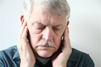 Not�cia: Disfun��o Temporomandibular (DTM). Descri��o da imagem: Homem idoso vestindo camisa social com as m�os nos ouvidos e olhando para baixo. Foto: Alice Day. Fim da descri��o.