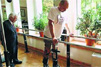 Not�cia: Homem paralisado volta a andar com terapia. Descri��o da imagem: A imagem mostra dois homens um segurando em dois corrim�es dando passos com um aparelho na perna e o outro ao fundo de terno observando. Est�o em uma sala fechada � luz do dia com plantas na janela. Foto: pol�cia federal/divulga��o. Fim da descri��o.