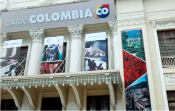 Galeria de imagens. Primeira imagem: Fotografia da parte superior da fachada de um prdio histrico, de cor amarelo-claro.  possvel ver duas grandes colunas no centro da fachada, que  simtrica, e vrios ornamentos nas janelas, colunas e beirais. Acima das colunas h um grande painel, cinzento, com os dizeres CASA COLOMBIA em branco, seguida por uma logomarca circular, nas cores amarelo, vermelho e azul, com a sigla CO. H, entre as colunas, painis com fotografias. Em um dos painis,  possvel ver a foto de vrias rosas vermelhas. Fim da descrio.
