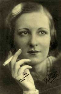 Foto de uma mulher fumando. Trata-se de Maria Victória Martinelli, que tornou-se companheira de Portinari pela vida toda. Ela aparece em close, segurando um cigarro com a mão direita. Os cabelos estão divididos para a esquerda e empastados à cabeça. O olhar dela não se direciona à câmera; as sobrancelhas e os lábios são finos e a mão tem os dedos entreabertos. 