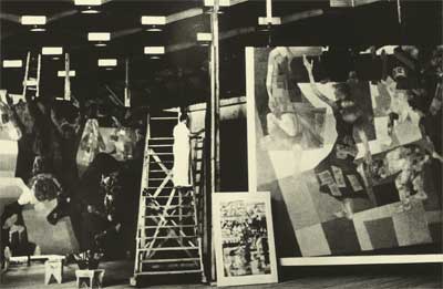 A foto está em preto e branco e apresenta imensas obras de Portinari. Em um local fechado, muito espaçoso e alto, há obras duas ou três vezes a altura média de uma pessoa. Entre as pinturas, percebe-se uma altíssima escada e um homem em pé sobre ela, vestido de branco. 