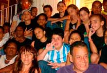 Nesta fotografia em cores, vê-se, em close, rostos de um grupo de crianças, acompanhadas por dois adultos. Nota-se que estão sentadas nos degraus de uma escada. A maioria dos integrantes infantis olham para a câmera sorrindo ou com uma expressão fechada.