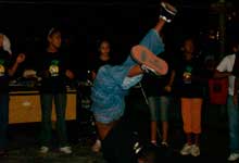 Nesta foto em cores e em close, vê-se um menino com as mãos no chão e as pernas para o alto. Atrás dele, há outros pré-adolescentes em pé, vestindo camisetas pretas.