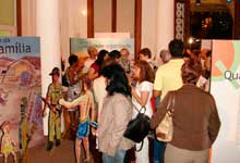 Nesta fotografia colorida, várias pessoas estão juntas em um salão onde há painéis da mostra. Os visitantes movimentam-se em diferentes direções. Observam-se os portais de acesso a outro ambiente, além de colunas redondas igualmente altos.