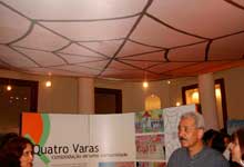 Nesta fotografia colorida, várias pessoas estão juntas em um salão onde há painéis da mostra. Observa-se que movimentam-se em diferentes direções. Notam-se ainda um dos painéis do projeto Quatro Varas e o desenho de uma enorme teia de aranha decorando o teto do salão.