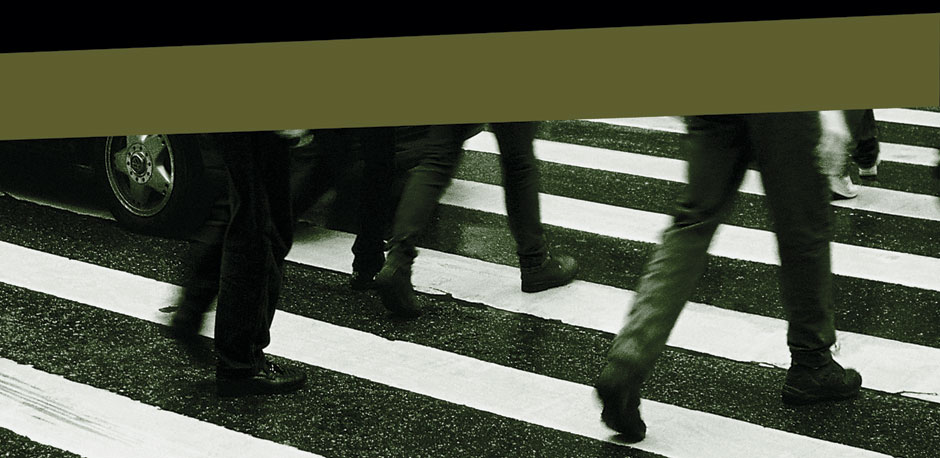 Nesta imagem em fundo preto, observa-se uma foto em preto e branco que mostra somente as pernas de pessoas caminhando sobre uma faixa de pedestres. 