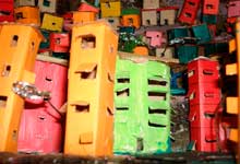 Esta foto em close revela espécie de maquete onde, imediatamente, se reconhece uma favela ou comunidade. Há casas e prédios coloridos, construídos desordenadamente, acompanhando o contorno do morro que ocupam.