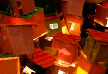 Esta foto em close revela espécie de maquete onde, imediatamente, se reconhece uma favela ou comunidade. Há casas coloridas, construídas desordenadamente, acompanhando o contorno do morro que ocupam.